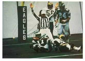 Full Color Carmichael scoring a touchdown with the Eagles in 1977. Jeno's - "1986 Jeno's Pizza - #6 Harold Carmichael". Jeno's. 1986. football card from the 1986 Jeno's Pizza NFL football card stickers set of Philadelphia Eagles wide receiver Harold Carmichael scoring a touchdown against the New Orleans Saints during a November 6, 1977 home game at Veterans Stadium. The card is numbered #6 in the set. The back of the card reads: THIS IS A FAMILIAR SIGHT Eagles wide receiver Harold Carmichael lands in the New Orleans Saints' end zone with one of the 79 touchdown passes he caught in his 14-year NFL career. The Philadelphia star also caught passes in 127 consecutive games to establish an NFL record, surpassing the old mark of 105 in 1979.