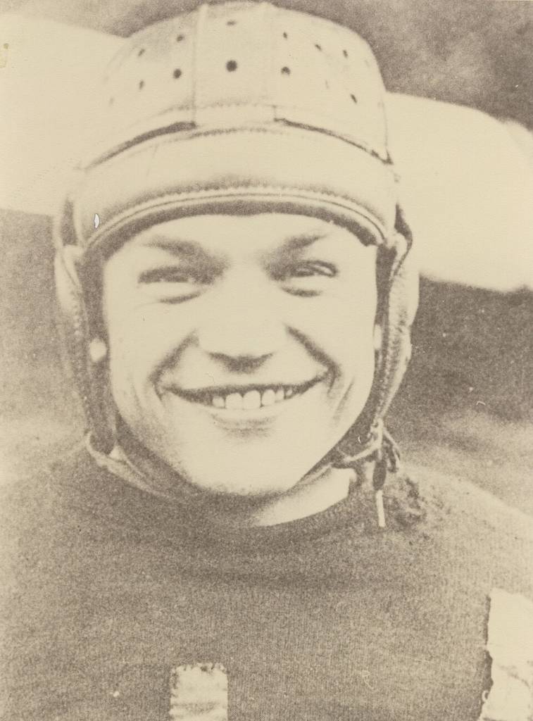 Vintage, yellowed, b/w image of Chic Harley in leather helmet and Ohio State football uniform, smiling.
