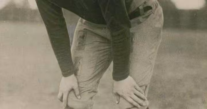 Vintage black and white publicity image of Ernie Nevers, Photo from Underwood & Underwood, Chicago, circa 1925. Nevers is posed hunched withhands on knees in full 1920s football gear.