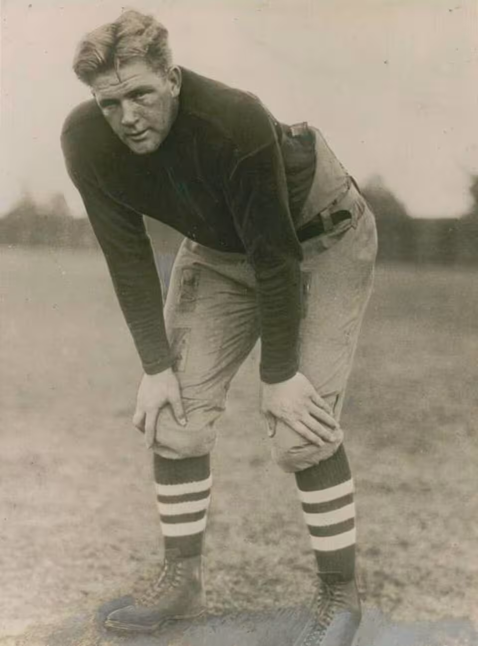 Vintage black and white publicity image of Ernie Nevers, Photo from Underwood & Underwood, Chicago, circa 1925. Nevers is posed hunched withhands on knees in full 1920s football gear.