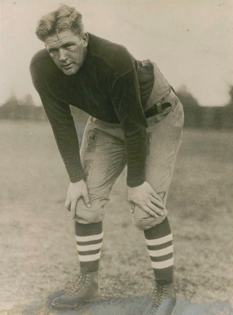 Vintage black and white publicity image of Ernie Nevers, Photo from Underwood & Underwood, Chicago, circa 1925. Nevers is posed hunched withhands on knees in full 1920s football gear.