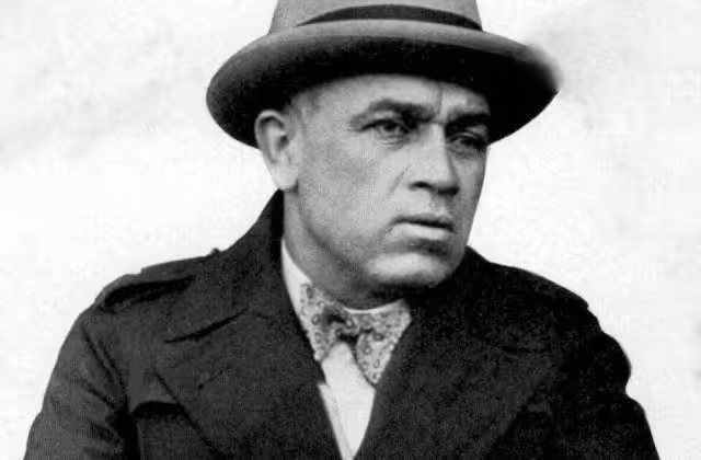 B/W image of John McGovern (cropped), in a fur coat and fedora.