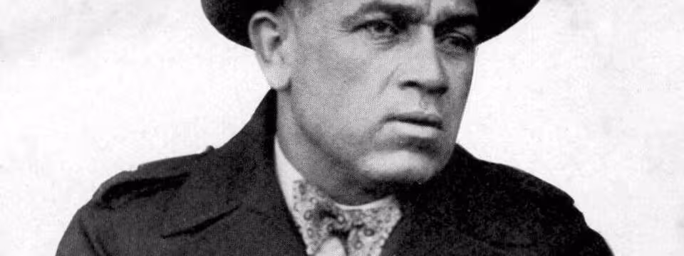 B/W image of John McGovern (cropped), in a fur coat and fedora.