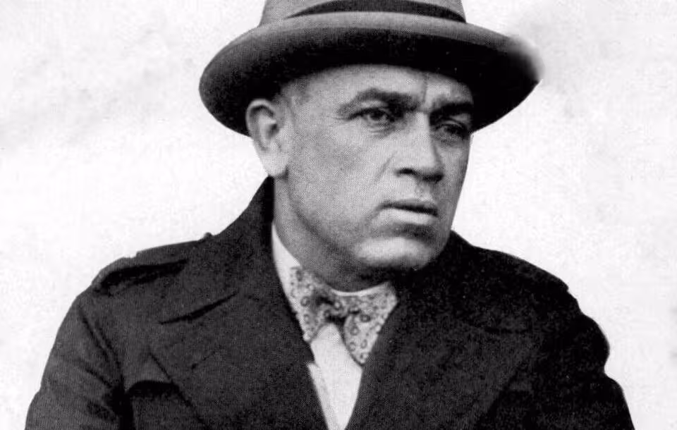 B/W image of John McGovern (cropped), in a fur coat and fedora.