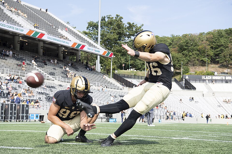 Color photo of an Army Cadets football player kicking from a hold.
