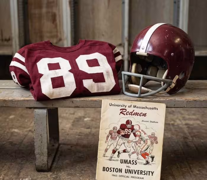Gemini AI-created image of a 1965-era University of Massachussetts American football jersey 89, without a name on it, and a matching period-correct helmet, the program cover appropriate to the era and team.