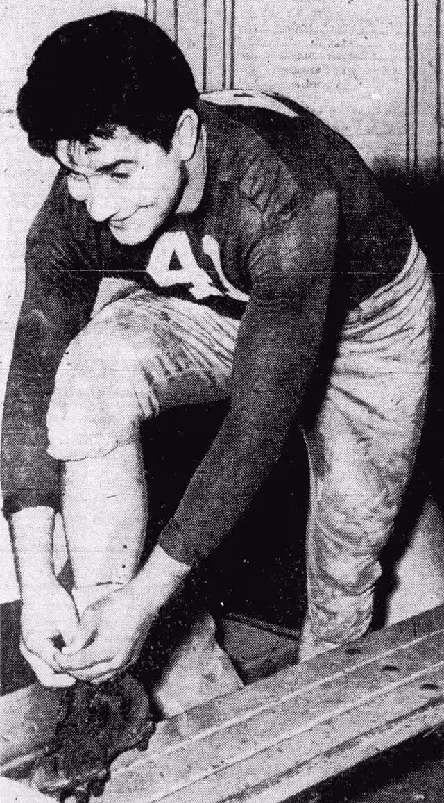 Black and white image of V. Mancha tying his show in the locker room wearing his dark number 41 jersey