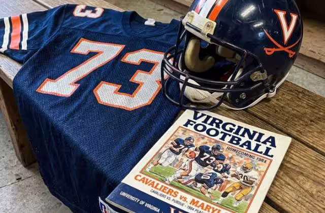 Gemini AI-created mage of a 1984-era University of Virginia American football jersey 73 jersey with silver numbers), without a name on it, and a matching period-correct helmet, the program cover appropriate to the era and team.