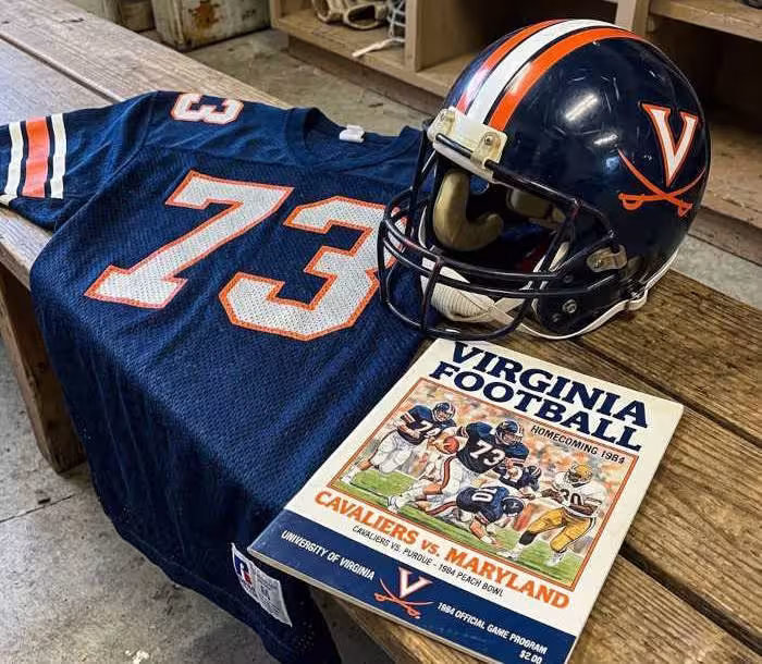 Gemini AI-created mage of a 1984-era University of Virginia American football jersey 73 jersey with silver numbers), without a name on it, and a matching period-correct helmet, the program cover appropriate to the era and team.