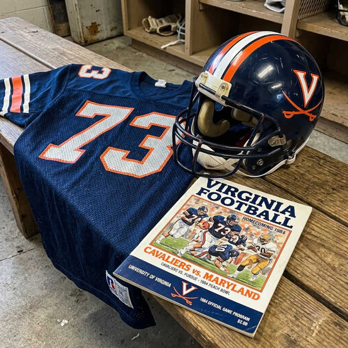 Gemini AI-created mage of a 1984-era University of Virginia American football jersey 73 jersey with silver numbers), without a name on it, and a matching period-correct helmet, the program cover appropriate to the era and team.