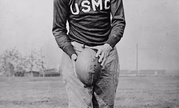 black and white 1915 era image of a publicity photo of a helmetless Eddie Mahan in his USMC uniform ready to punt