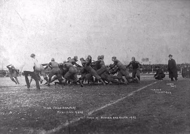 b/w image of game action in game between the Minnesota Golden Gophers and the Michigan Wolverines football teams.