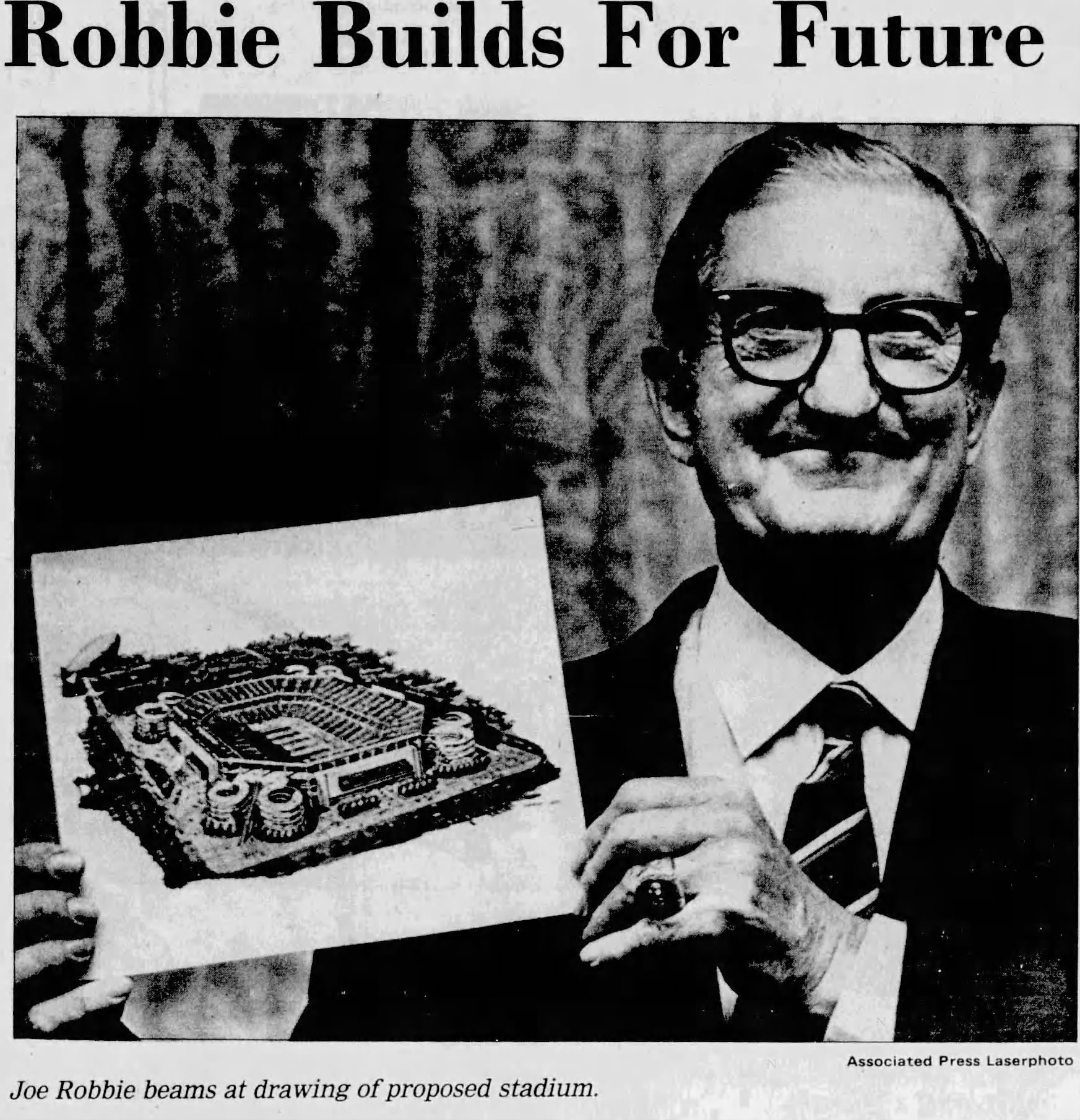b/w newspaper image of former Dolphins owner Joe_Robbie_1985 holding up a picture a proposed new football stadium rendering