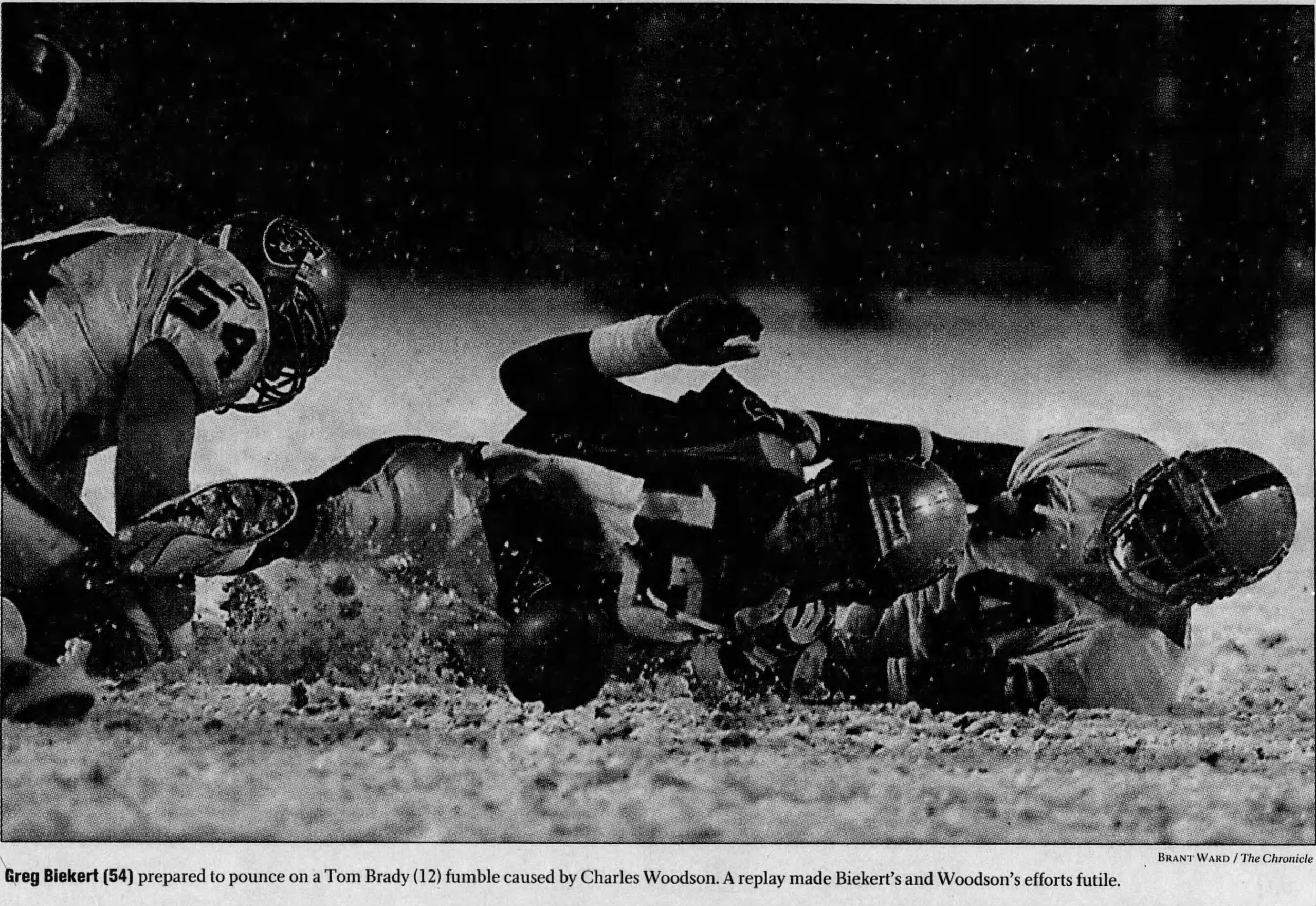 b/w newspaper image of Tome Brady' on the ground with Charles Woodson with a loose ball on the ground int he snow.