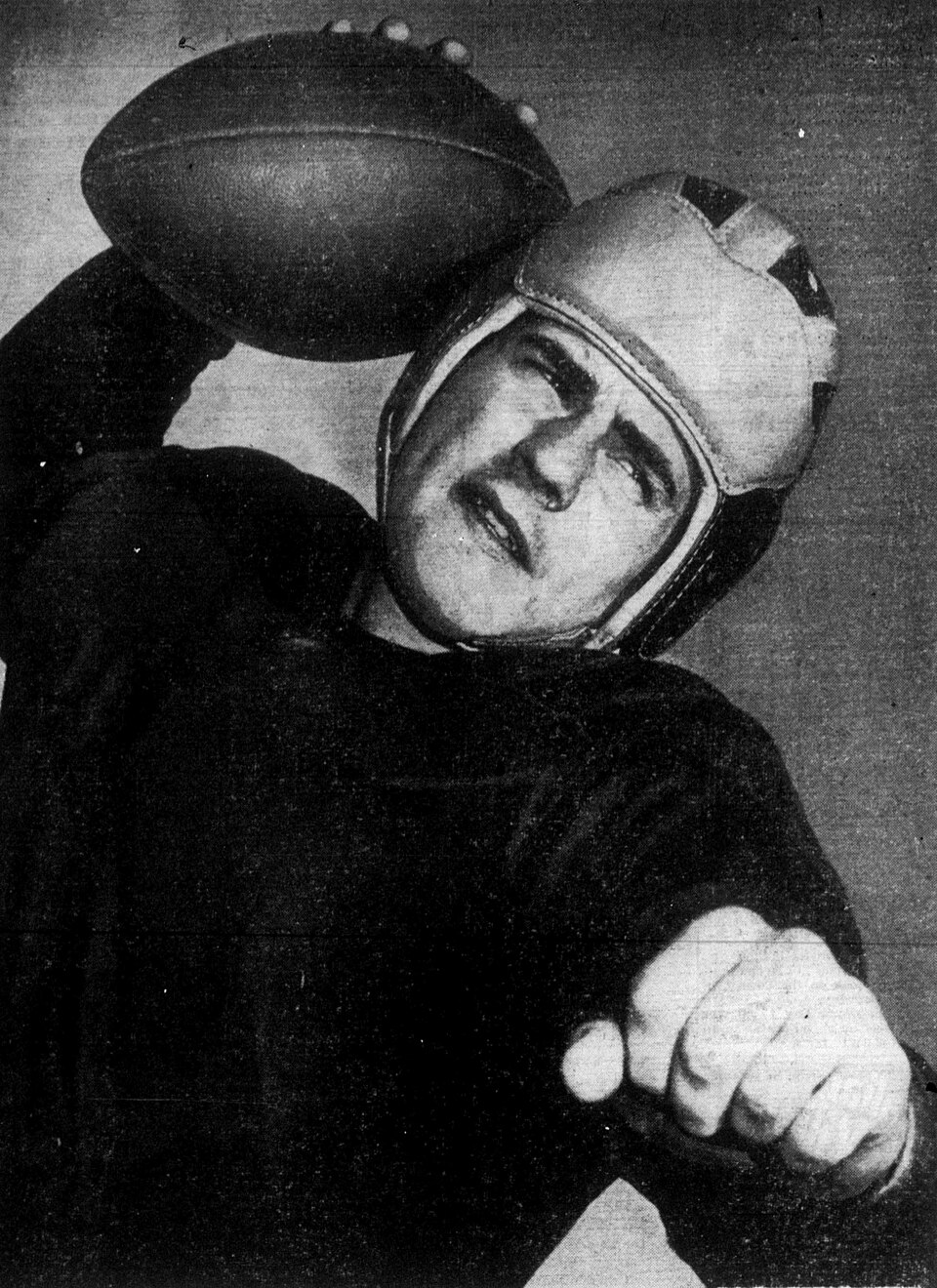 black and white action photo pose of merican football player Bob Chappuis, 1947, holding a football, wearing a leather helmet