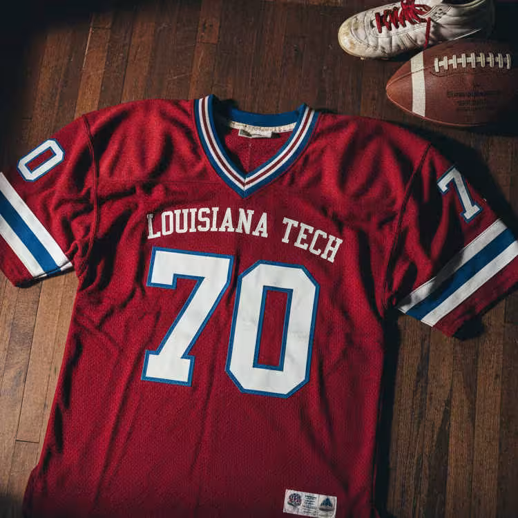 Image of a red LA Techfootball Jersey number 70 with a football helmet and old cleats.