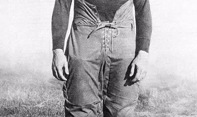 black and white full image of ND star George Gipp in full 1920s era football gear standing on a playing field