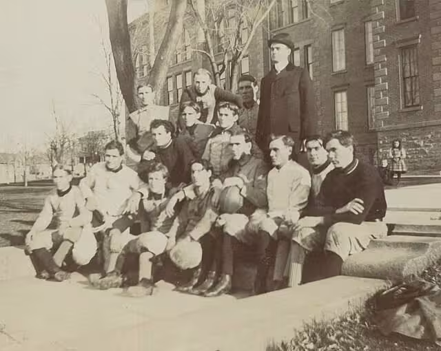 black and white team photo of Mankato State Normal School 1898 Football Team in front of a brick building