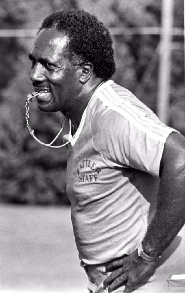 black and white image of coach Rudy Hubbard with a whistle in his mouth, 1983
