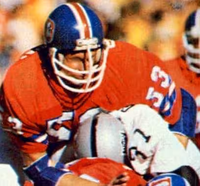 game action image of an orange clad Randy Gradishar tackling an Oakland runner