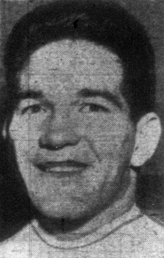 A grainy, black-and-white newspaper-style headshot of Billy Vessels, the 1952 Heisman Trophy winner. He is shown from the shoulders up, wearing a light-colored crew-neck athletic shirt. He has short, dark hair and a wide, friendly smile. The image captures the high-contrast texture of mid-century newsprint photography.