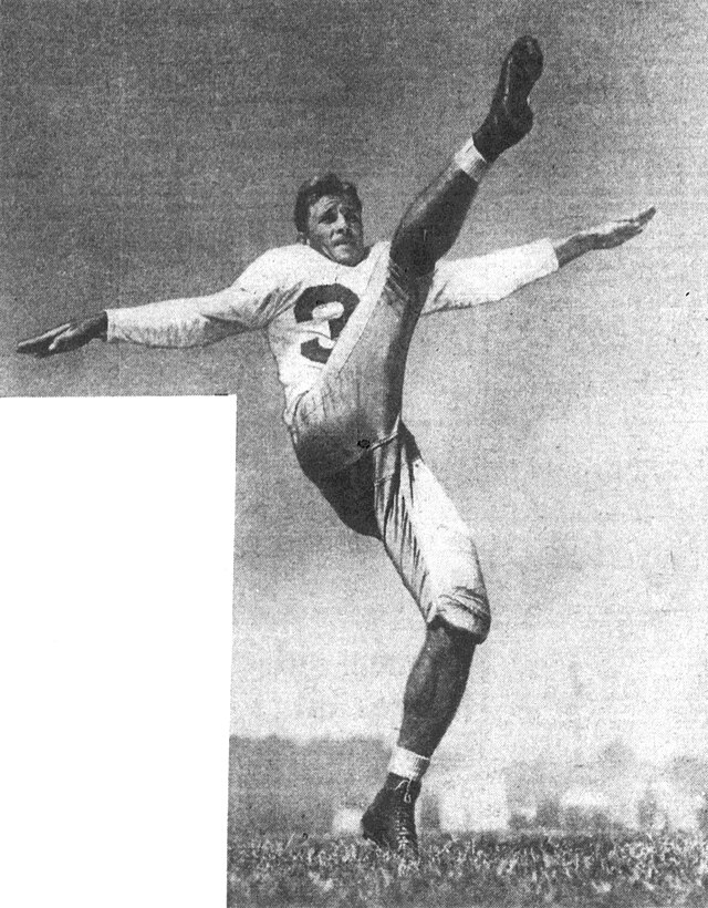 A black-and-white action photograph of SMU legend Doak Walker from 1947. He is captured mid-air in a high-kicking punting follow-through, his right leg extended vertically. He is wearing a white jersey with a dark number '37,' light-colored padded football pants, and high-top cleats against an open-field background.