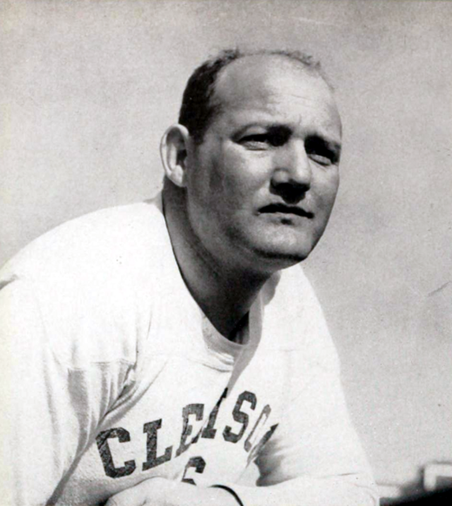 A black-and-white portrait of legendary Clemson football coach Frank Howard, as featured in the 1941 edition of the 'Taps' yearbook. Howard is shown in a three-quarter view, leaning forward with a focused expression. He is wearing a white Clemson jersey with the team name arched across the chest in dark block letters. The lighting is natural, casting soft shadows across his face against a pale, open background.
