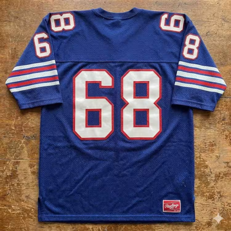 A flat-lay photograph of a deep blue mesh football jersey on a rustic wooden surface. The jersey features the number '68' in large white block digits with a red outline. The sleeves include red and white horizontal stripes, and a red Rawlings jock tag is visible at the bottom right hem.