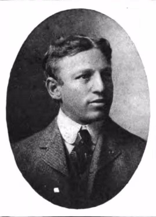 A black-and-white oval studio portrait of Philip King, a Hall of Fame quarterback and legendary football coach. He is depicted from the shoulders up, wearing a formal tweed suit jacket, a high-collared white shirt, and a dark patterned tie. He has short, wavy hair and is looking off-camera with a serious expression.