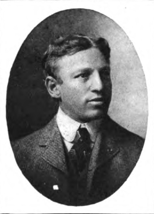 A black-and-white oval studio portrait of Philip King, a Hall of Fame quarterback and legendary football coach. He is depicted from the shoulders up, wearing a formal tweed suit jacket, a high-collared white shirt, and a dark patterned tie. He has short, wavy hair and is looking off-camera with a serious expression.