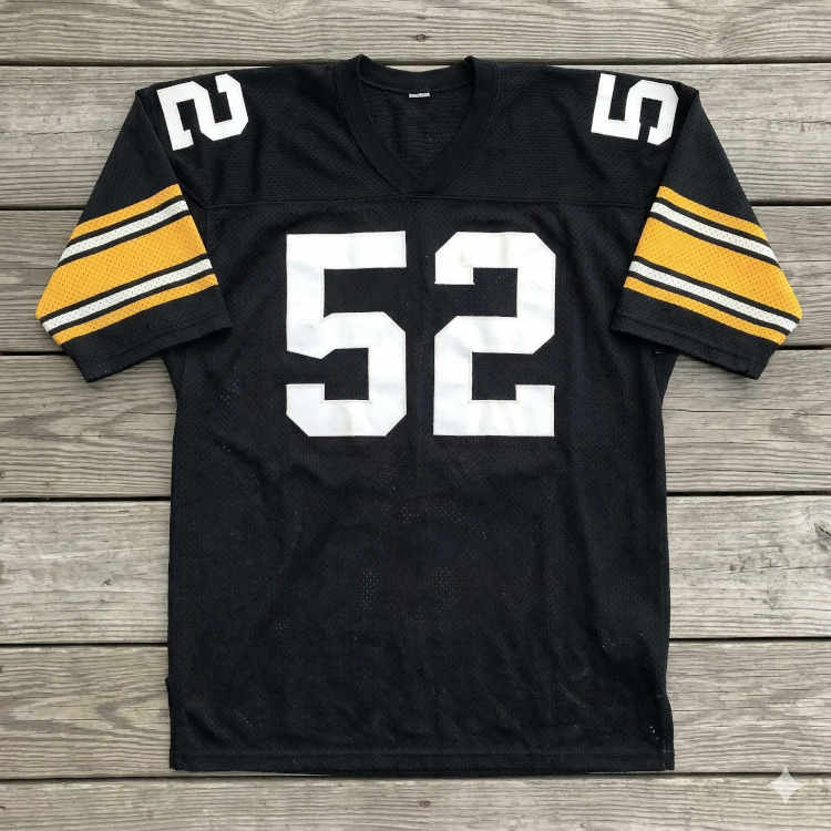 A flat-lay photograph of a black mesh football jersey displayed on a grey wooden deck. The jersey features the number '52' in large white block digits on the chest and shoulders. The sleeves are accented with broad gold horizontal bands, each containing two thin black and white stripes.