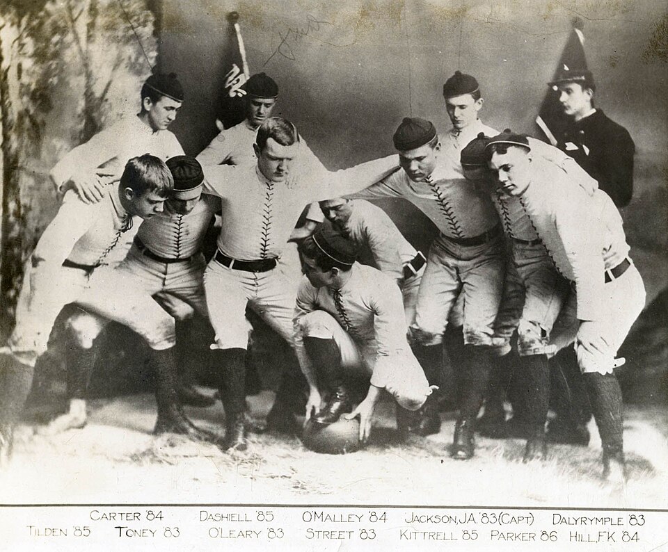 Vintage black and white team photo of A posed image of the 1882 United States Naval Academy football team, lined up in their positions as if they were about to start a play.