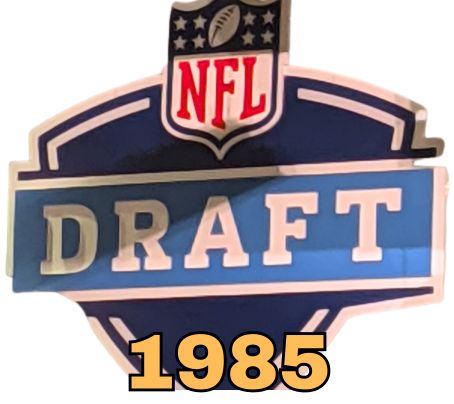 NFL Draft sign in color on a white background with the year 1985 text across the bottom in bright orange. The original cropped image was taken by Darin Hayes at AT&T Stadium in 2022.