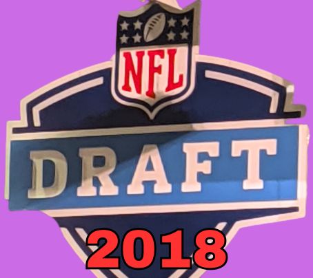 NFL Draft sign in color on a purple background with the year 2018 text across the bottom in red. The original cropped image was taken by Darin Hayes at AT&T Stadium in 2022.