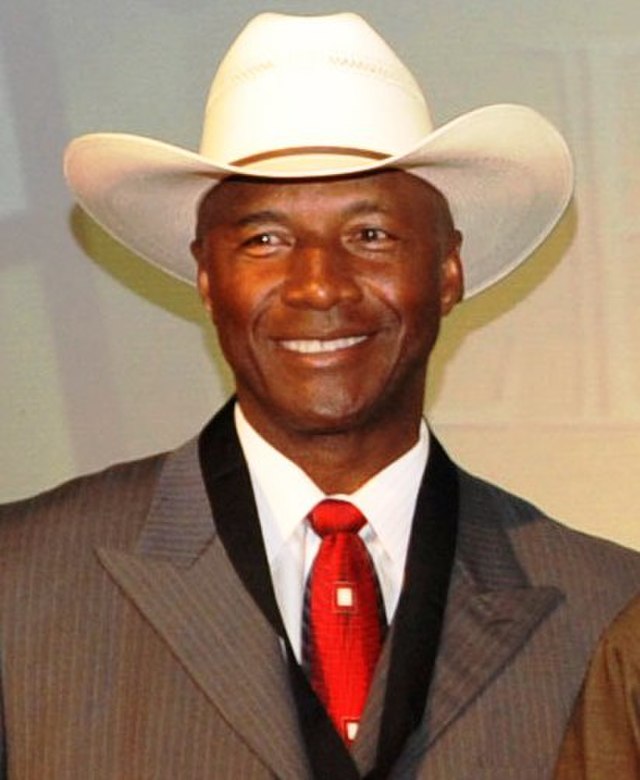 Archival photograph of Pittsburgh Steelers legend Mel Blount. Blount is shown smiling in a grey suit, red tie, and white cowboy hat. A primary source for historical research into the 1970s Steel Curtain defense and NFL rule changes for Pigskin Dispatch archives.