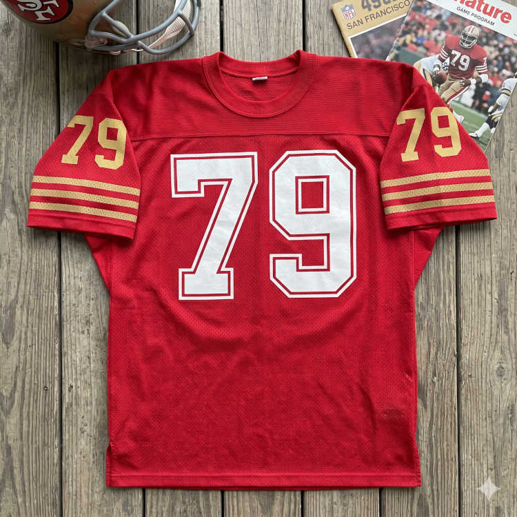 Vintage San Francisco 49ers #79 football jersey. Red mesh with solid white block numbers and gold-striped sleeves. Features 1980s 49ers game program and gold helmet for historical NFL dynasty research and Pigskin Dispatch archives.