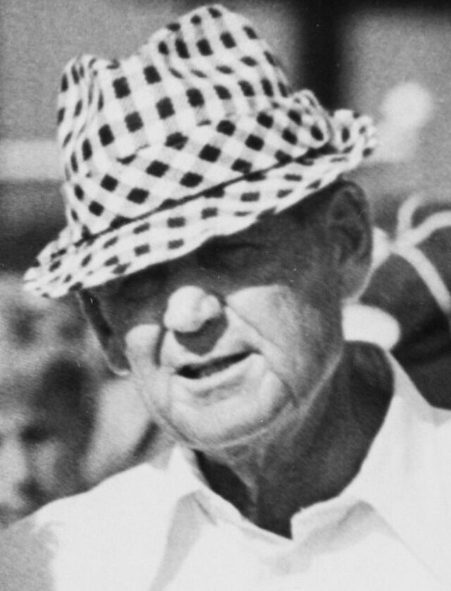 Vintage 1977 cropped photograph of Alabama head coach Paul 'Bear' Bryant. Bryant is shown in his signature houndstooth hat and a white polo shirt, gazing intently at the field for historical SEC football research and Pigskin Dispatch archives.