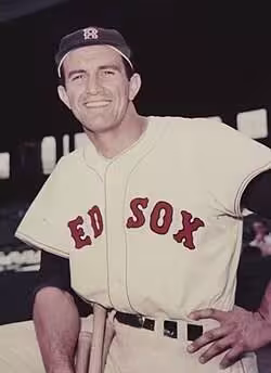 Vintage color archival portrait of Boston Red Sox first baseman and Boston University football legend Harry Agganis. Features Agganis in a cream Red Sox home uniform at Fenway Park. A primary source for multi-sport athlete research and New England sports history for Pigskin Dispatch archives.