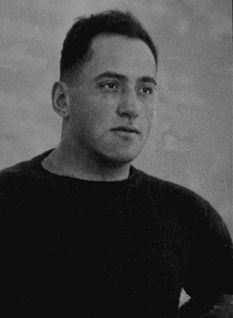 A black-and-white archival portrait of Joseph 'Doc' Alexander. He is shown from the chest up, wearing a dark, long-sleeved wool football jersey typical of the late 1910s and early 1920s. He has short-cropped hair and a stoic, focused expression. The background is a neutral, light-colored gradient, common in vintage athletic portraiture.