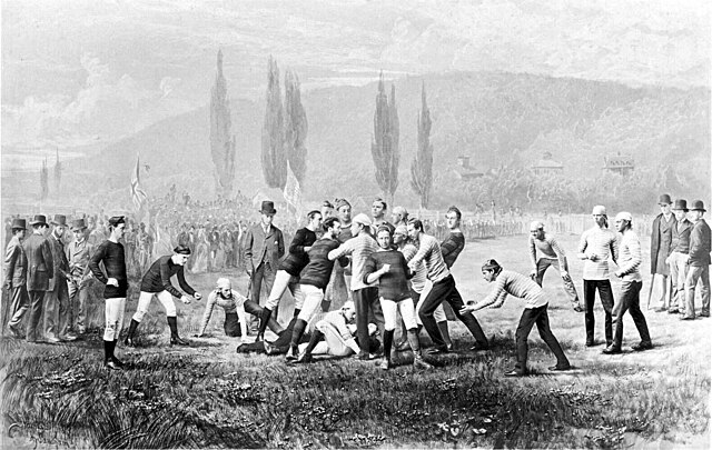 The illustration depicts a mass-momentum scrum, a hallmark of 19th-century play that relied on collective physical force rather than the specialized tactical positioning seen in modern gridiron. Players are shown in varying uniforms—striped jerseys and dark wool sweaters—vying for control of a prolate spheroid ball that had not yet been standardized to the modern "Duke" shape. In the background, spectators in formal 19th-century attire (including top hats and overcoats) watch from the sidelines, illustrating the sport's high-society collegiate roots.