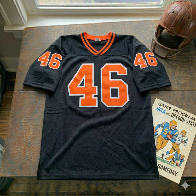 Vintage Oregon State Beavers #46 football jersey. Black mesh with orange and white shadowed block numbers. Features 1960s UCLA vs. Oregon State game program and vintage leather wing helmet for historical Pac-12 sports research and Pigskin Dispatch archives.