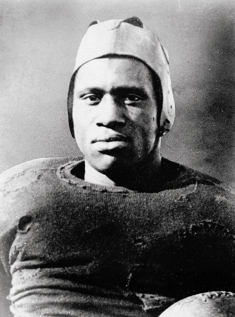 Vintage archival photo of Paul Robeson as an All-American football player for Rutgers. Robeson is shown in a worn wool jersey and primitive leather helmet, gazing forward with intense focus for historical sports research and Pigskin Dispatch archives.