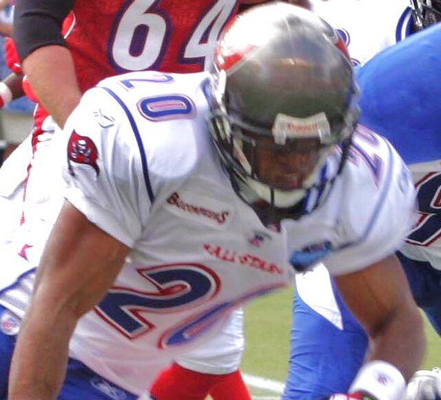 Close-up action photo of Tampa Bay Buccaneers cornerback Ronde Barber #20 at the 2006 Pro Bowl. Barber is shown in a white NFC All-Stars jersey with Buccaneers shoulder patch and dark Riddell helmet for historical NFL research and Pigskin Dispatch archives.