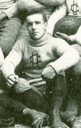 Vintage 1889 archival photograph of Cornell football halfback Winchester Osgood. Black and white portrait of Osgood in a light-colored turtle-neck sweater with an interlocking CC logo, sitting on the floor with a 1889 Cornell football for historical sports research and Pigskin Dispatch archives.