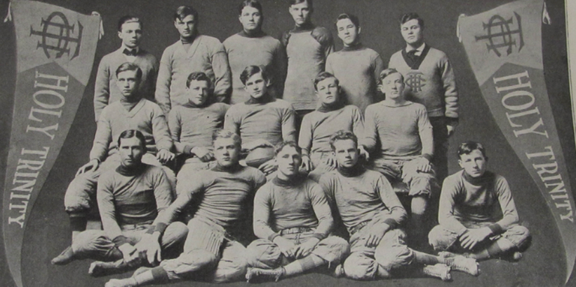 Vintage black and white team photo of Holy Trinity Hilltoppers football team. Coach Utay top right