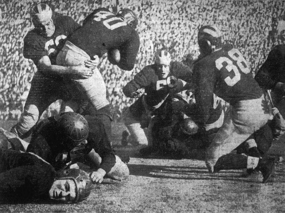Vintage black and white game action photo of USC Trojans football player Newell Oestreich (number 40, with ball) is tackled by Michigan Wolverines defender Joe Soboleski (number 69) during the 1948 Rose Bowl Game on January 1 in Pasadena, California. USC player Mickey McCardle in seen in the far right of the foreground with head head on the turf.