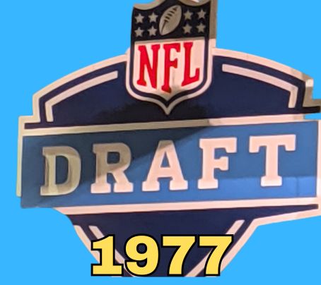 NFL Draft sign in color on a blue background with the year 1977 text across the bottom in yellow. The original cropped image was taken by Darin Hayes at AT&T Stadium in 2022.