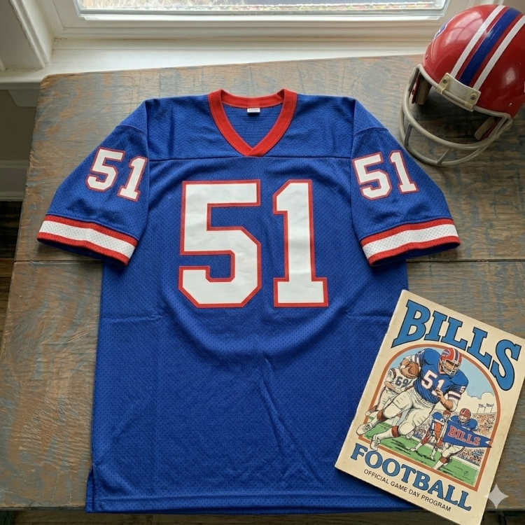 Vintage Buffalo Bills #51 football jersey as seen in Bills_51.jpg. Royal blue mesh with white and red shadowed block numbers. Includes a red Bills helmet with the charging buffalo logo and a vintage gameday program for historical NFL research for Pigskin Dispatch archives.