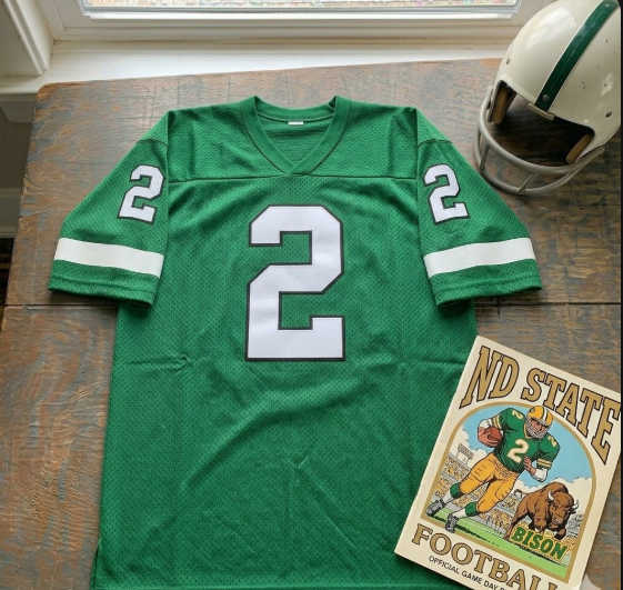 An AI generated Green number 2 football jersey sitting on a table with a white football helmet and a ND State Bisons program