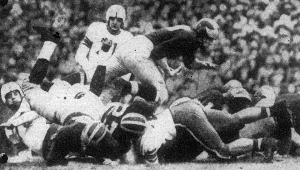 Vintage black and white still photo of game action of Michigan Wolverines halfback Chuck Ortmann (center, with ball) picks up five yards during a game against the Ohio State Buckeyes on November 19, 1949 at Michigan Stadium in Ann Arbor, Michigan.